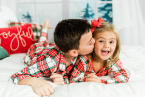 Brother kissing sister's cheek in matching Christmas pajamas during studio session