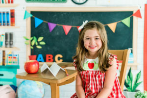 Girl in apple-print dress posing in back-to-school studio setup in Kingston