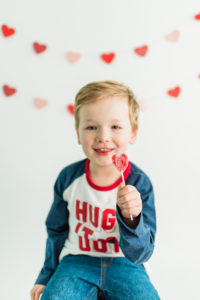 Boy holding Valentine's sucker in front of heart backdrop in Kingston studio