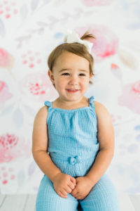 Toddler girl in blue outfit posing with floral backdrop in Kingston studio
