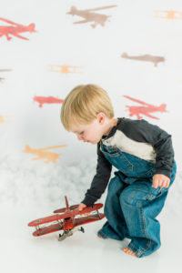 Boy playing with toy airplanes in front of airplane backdrop in Kingston studio