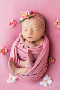 Newborn baby girl in a wrap showing hands and feet on pink floral backdrop, Knoxville newborn photography