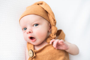 Newborn baby boy in orange overalls and matching sleeping cap, Knoxville newborn photography
