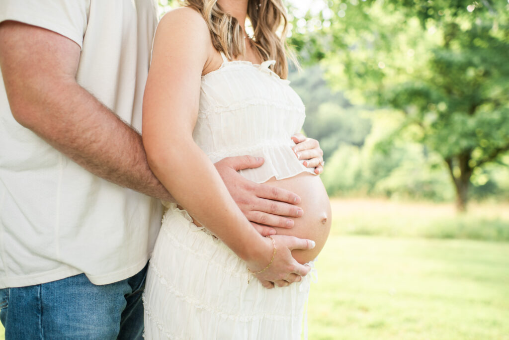 Expecting couple holding hands on the baby bump at Lakeshore Park in Harriman, TN
