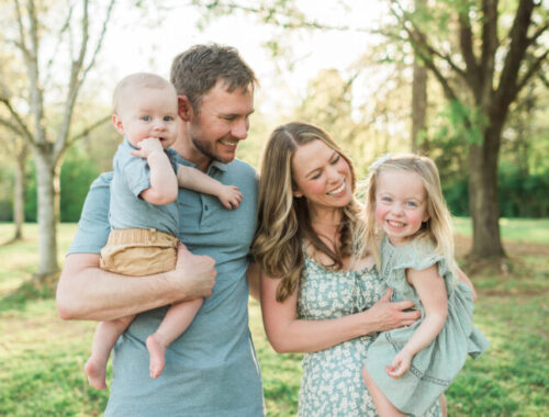 Family of four smiling as parents hold their two young children at golden hour in a Knoxville, TN park