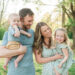 Family of four smiling as parents hold their two young children at golden hour in a Knoxville, TN park