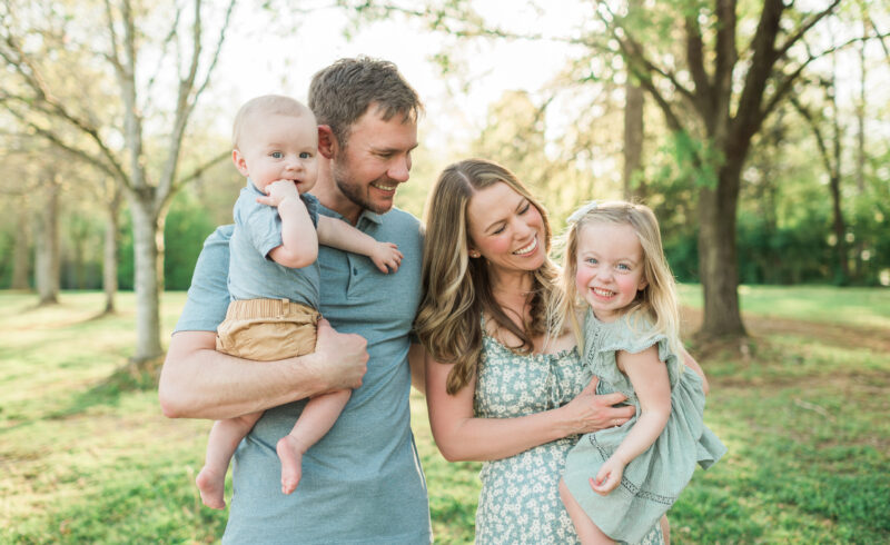 Family of four smiling as parents hold their two young children at golden hour in a Knoxville, TN park