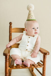 Baby boy in rocking chair wearing half birthday hat during neutral studio session