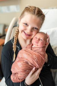 Mom smiling at camera while holding newborn baby during Fresh 48 hospital session