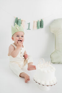 Boy with crown celebrating first birthday with "one" banner and green and cream backdrop