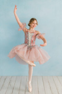 Young ballerina posing on pointe shoes in front of light blue backdrop in Kingston studio