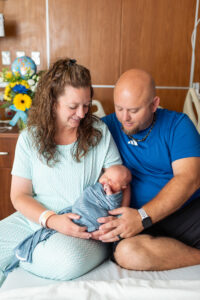 Mom and dad together in hospital bed holding and looking at newborn baby during Fresh 48 session