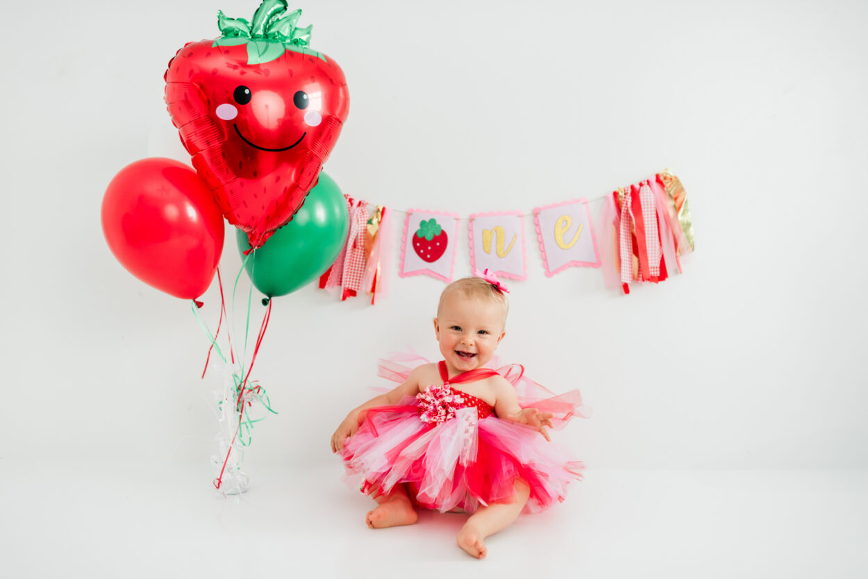 Girl in strawberry dress celebrating first birthday with "one" banner in Kingston studio
