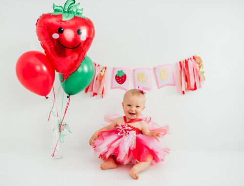 Girl in strawberry dress celebrating first birthday with "one" banner in Kingston studio