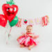 Girl in strawberry dress celebrating first birthday with "one" banner in Kingston studio