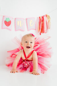 Girl in strawberry dress celebrating first birthday with "one" banner in Kingston studio