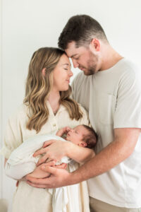 New parents holding their sleeping newborn son together in neutral outfits during a Knoxville newborn photography session
