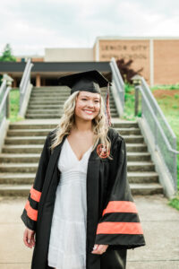 Close-up portrait of smiling senior in cap and gown on the steps of Lenoir City High School