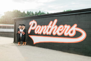 Seniors in caps and gowns posing beside the Panthers mascot mural at their high school