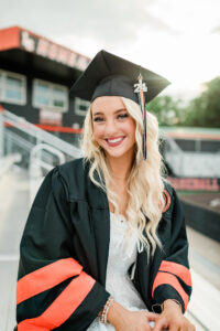 Close-up of smiling senior in black cap with orange tassel at the Lenior City High School football stadium