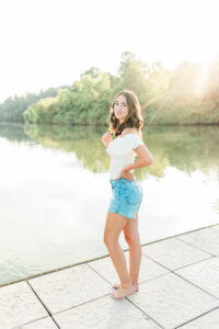 Knoxville senior photographer captures barefoot senior in white top and denim shorts at sunset by the lake