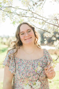 Senior girl in floral dress and glasses smiling under white spring blossoms, Knoxville senior photographer portrait