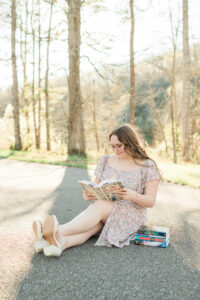Senior girl sitting outdoors reading a book beside a stack of novels, styled senior session by Knoxville senior photographer