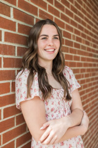 Senior girl in pink floral dress leaning against a red brick wall, Knoxville senior photographer portrait session
