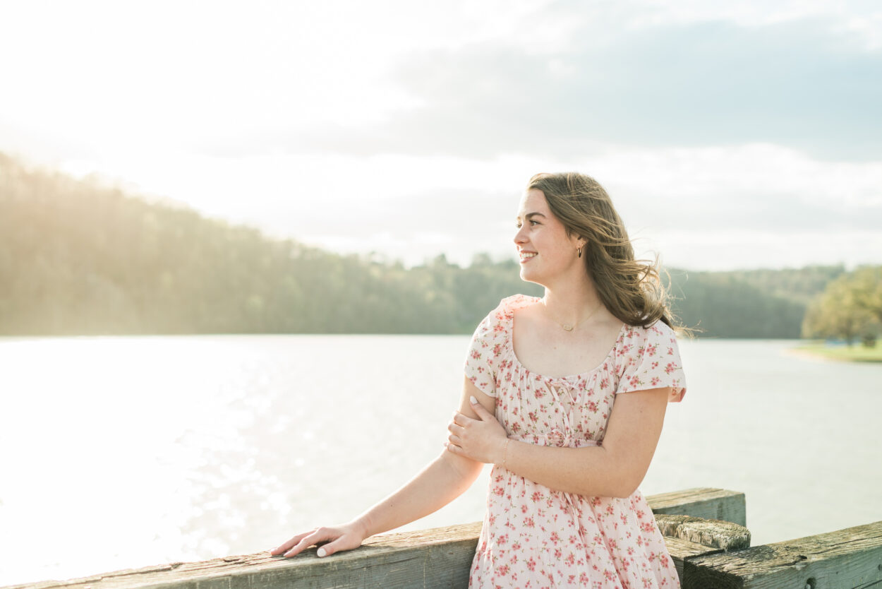Senior girl in pink floral dress standing by a lake at golden hour, Knoxville senior photographer lakeside session