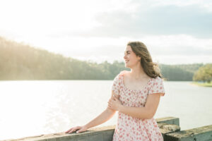 Senior girl in pink floral dress standing by a lake at golden hour, Knoxville senior photographer lakeside session