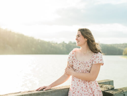 Senior girl in pink floral dress standing by a lake at golden hour, Knoxville senior photographer lakeside session