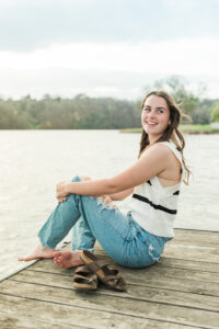 Senior girl in striped sweater and ripped jeans sitting barefoot on a lake dock, Knoxville senior photographer portrait