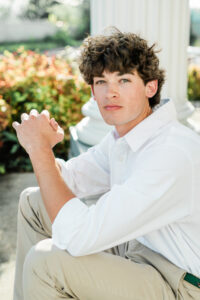 enior guy in white button-down shirt sitting outdoors near white columns, Knoxville senior photographer portrait