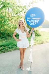 Senior holding a large blue balloon reading Middle Tennessee Women's Golf, celebrating her college commitment