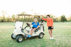Senior in MTSU t-shirt sitting in a golf cart on a golf course with a friend in Carson-Newman shirt