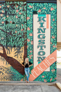 Senior in black top leaning against colorful Kingston peaches mural in downtown Kingston Tennessee