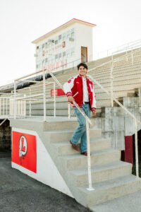 Senior smiling and walking down bleacher steps in red and white varsity letterman jacket