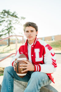 Close-up portrait of senior in letterman jacket holding a football in golden sunlight