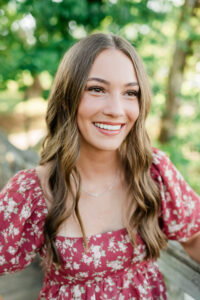 Close-up portrait of smiling senior in pink floral dress with green forest background