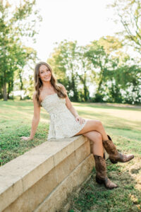 Senior in floral dress and cowboy boots sitting on a stone wall in a park